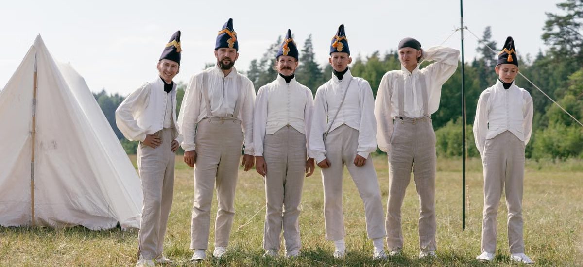 A group of soldiers in historical uniforms standing in a field beside a tent.