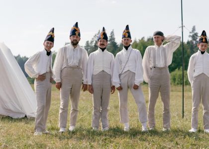 A group of soldiers in historical uniforms standing in a field beside a tent.