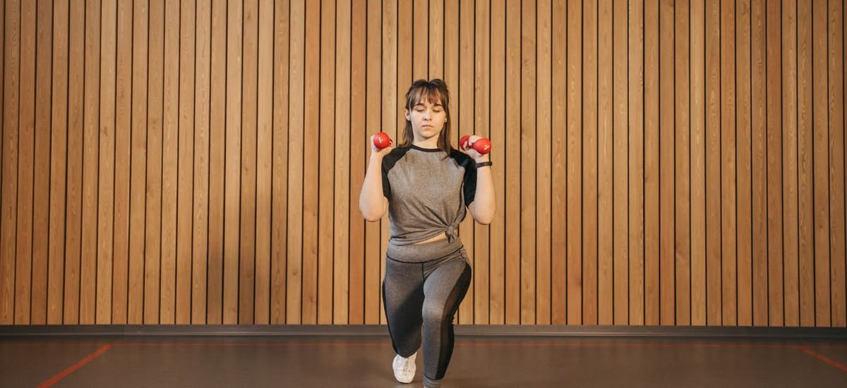 A woman performing lunges with dumbbells in a modern indoor gym setting.