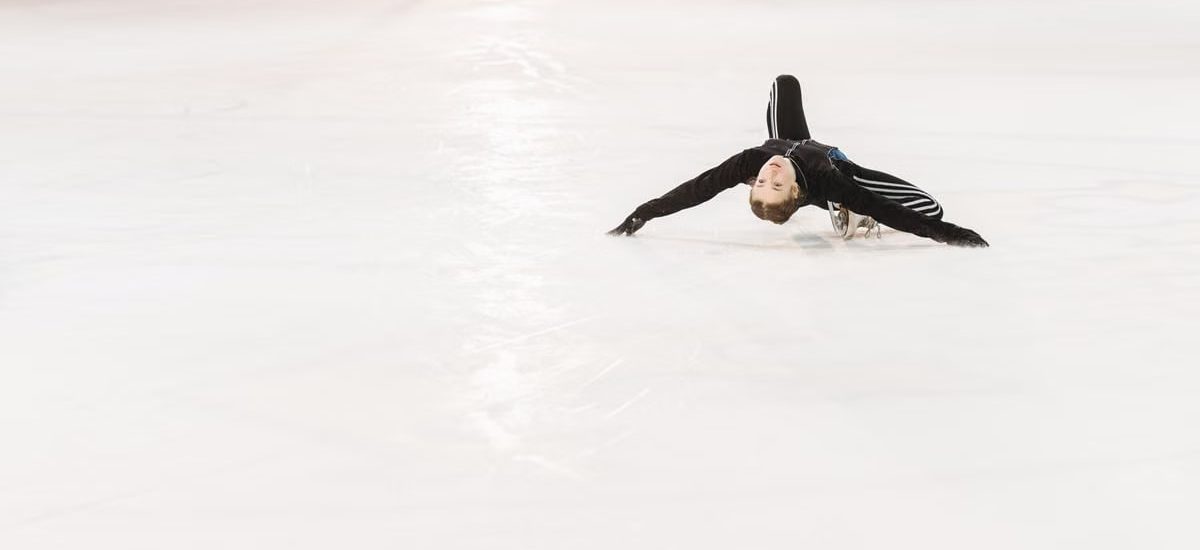 A talented young figure skater performs a creative pose on an indoor ice rink.