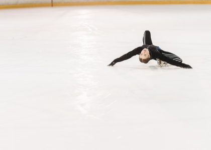 A talented young figure skater performs a creative pose on an indoor ice rink.